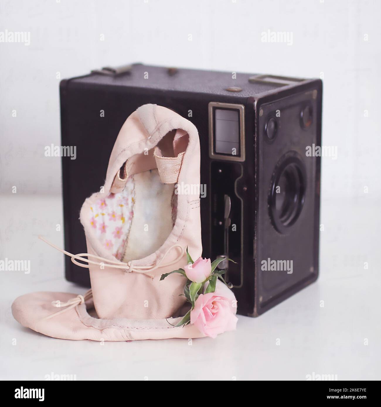 A little ballerina girls first pair of ballet slippers are propped up on a vintage film camera with the tiny pink roses from her first dance recital Stock Photo