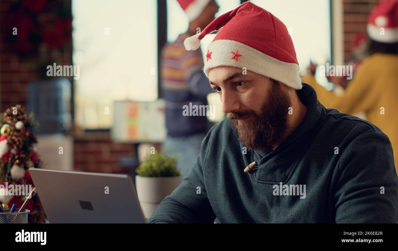 Frustrated man being interrupted by noisy coworkers celebrating winter holiday season. Tired person feeling irritated and disturbed because of festive people making noise during christmas time. Stock Photo