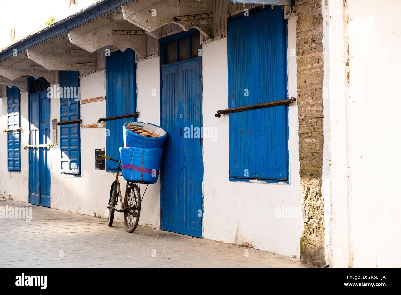 Old bicycle leaning against a white & indigo blue building carrying baskets filled with Khobz, the Moroccan round bread typically eaten with tagine Stock Photo