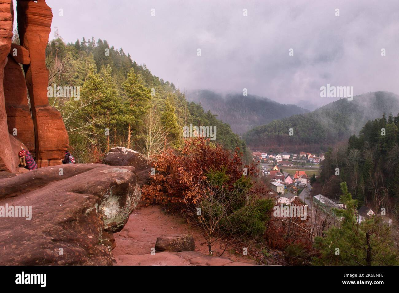 Hinterweidenthal, Germany - January 1, 2021: Kids climbing on red rocks at Devil's Table overlooking a small village in Germany on a foggy winter day. Stock Photo