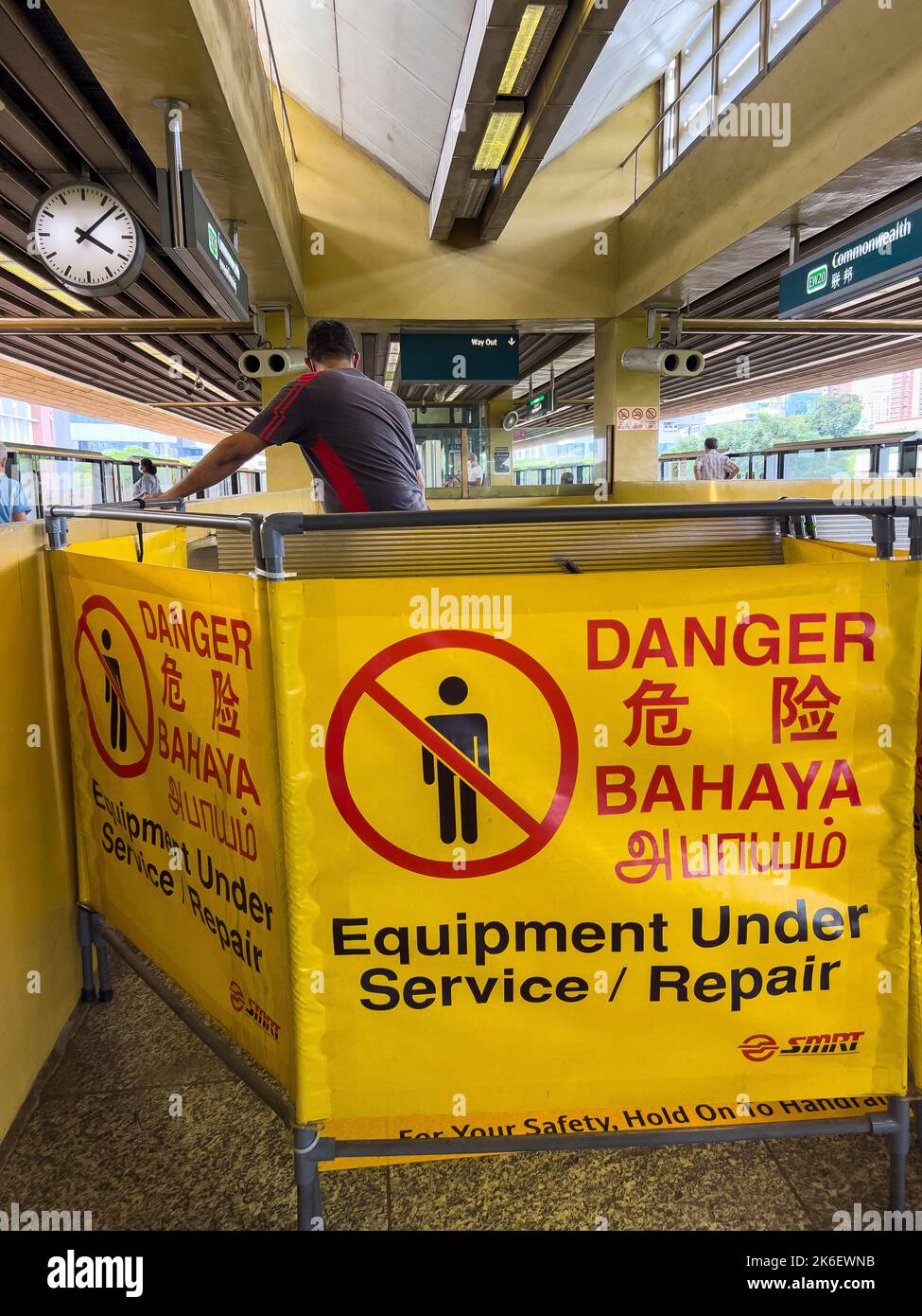 Escalator is closed for repair at train station, danger sign is put up to inform the public. A professional service staff is doing the work. Stock Photo