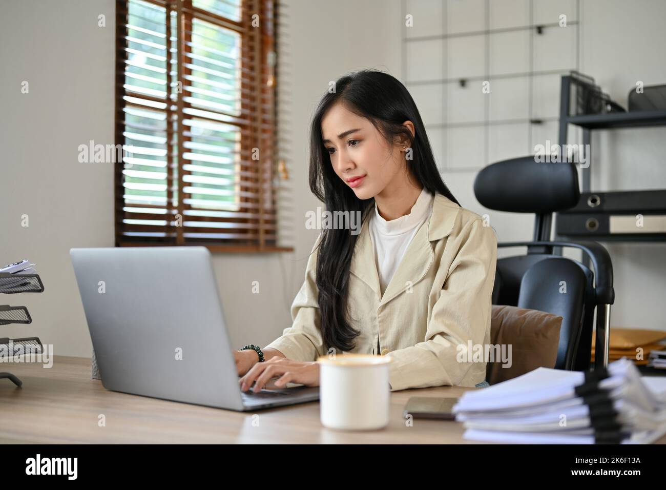 Confident and successful young Asian businesswoman or female manager concentrating on her work on laptop computer, managing her tasks on laptop, typin Stock Photo
