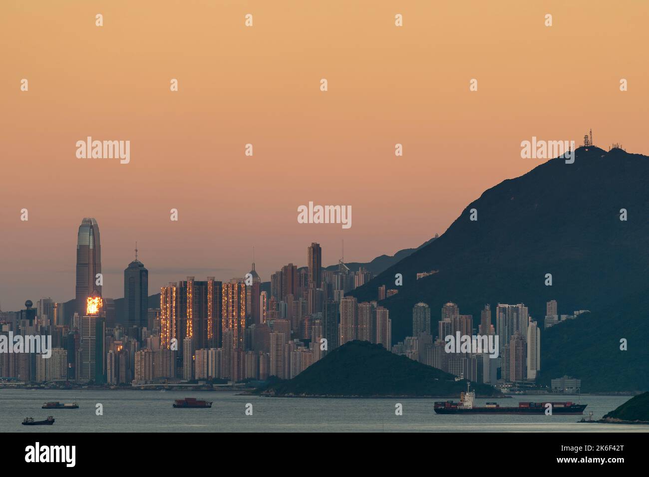 The setting sun is reflected in the high-rise buildings of Hong Kong Island, seen against the orange sky of the Belt of Venus phenomenon Stock Photo