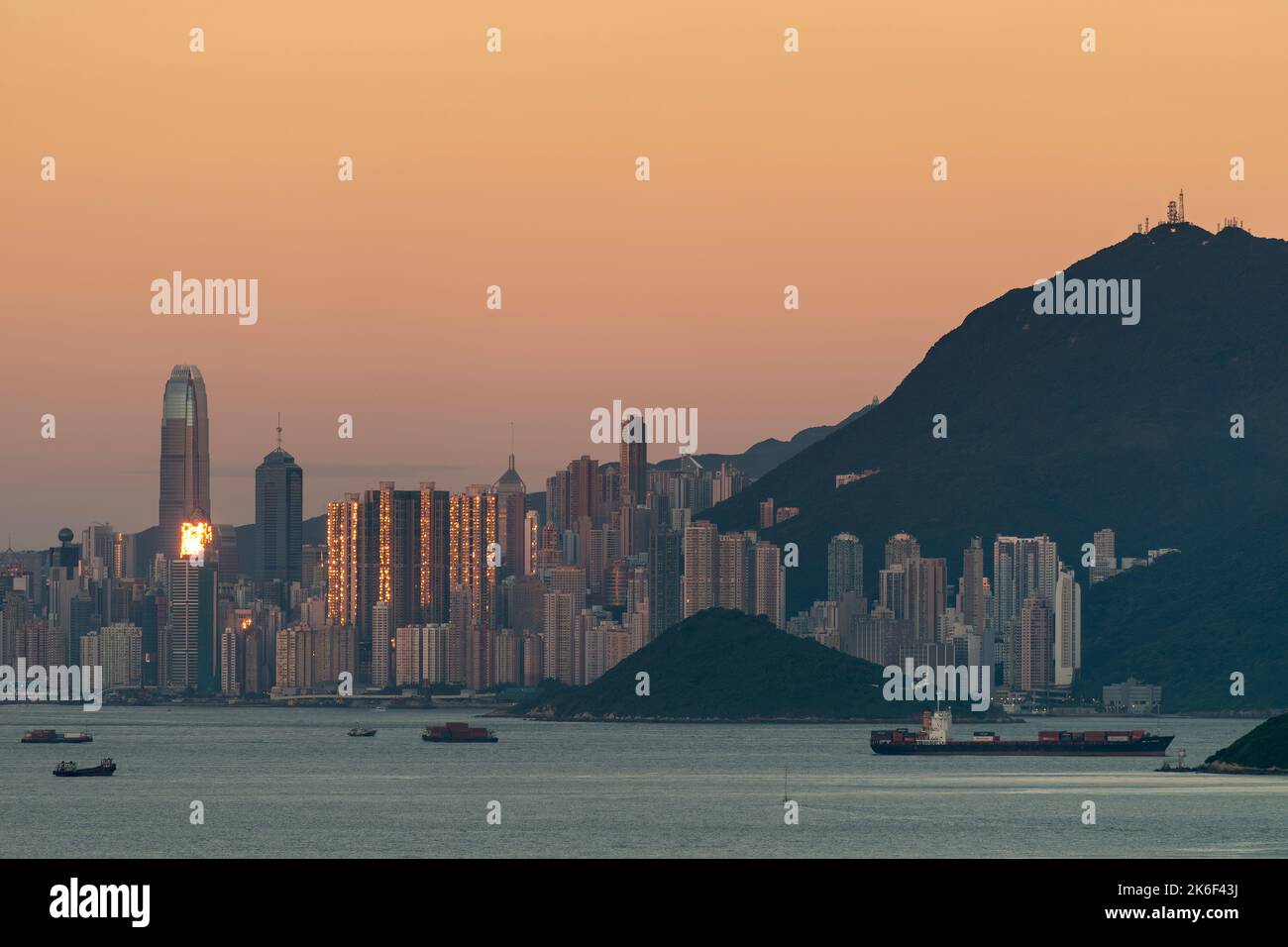 The setting sun is reflected in the high-rise buildings of Hong Kong Island, seen against the orange sky of the Belt of Venus phenomenon Stock Photo