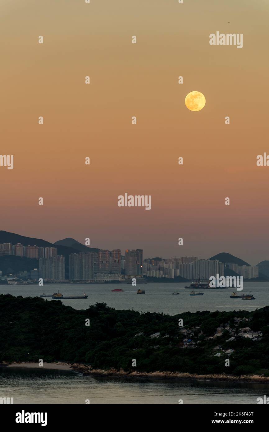 The full moon rises through the orange eastern sky, with the setting sun reflected in the high-rise buildings of Pol Fu Lam, Hong Kong Island Stock Photo