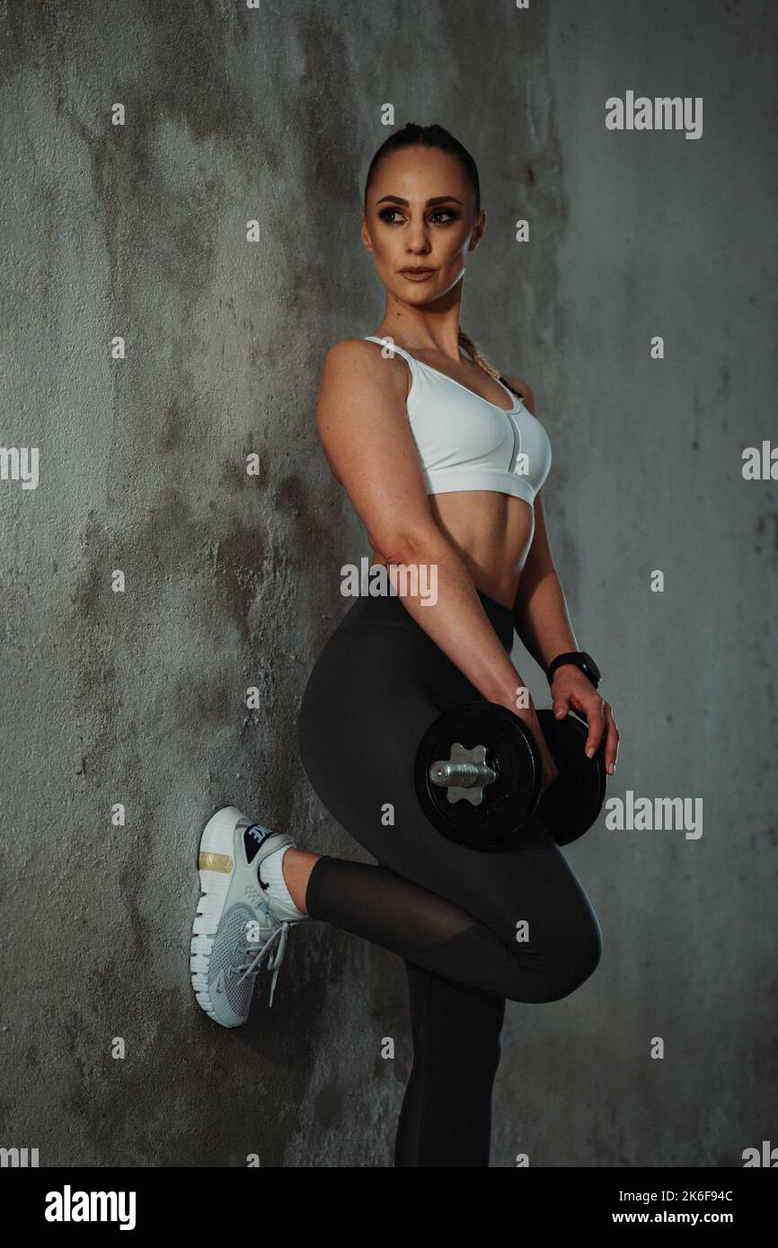 Sporty young girl leaning her left leg on the wall, lookingright