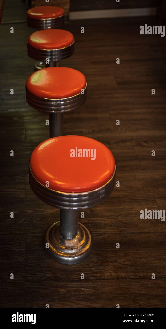 Vintage stools in the restaurant. Row vintage stools in front of wooden counter inside a vintage style bar. A row of four shiny red vinyl stools. Nobo Stock Photo