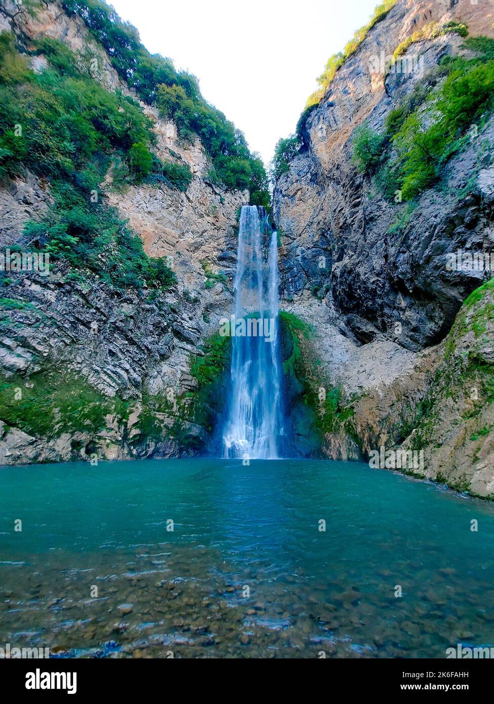 A vertical shot of the waterfall flowing between the rocky formations ...