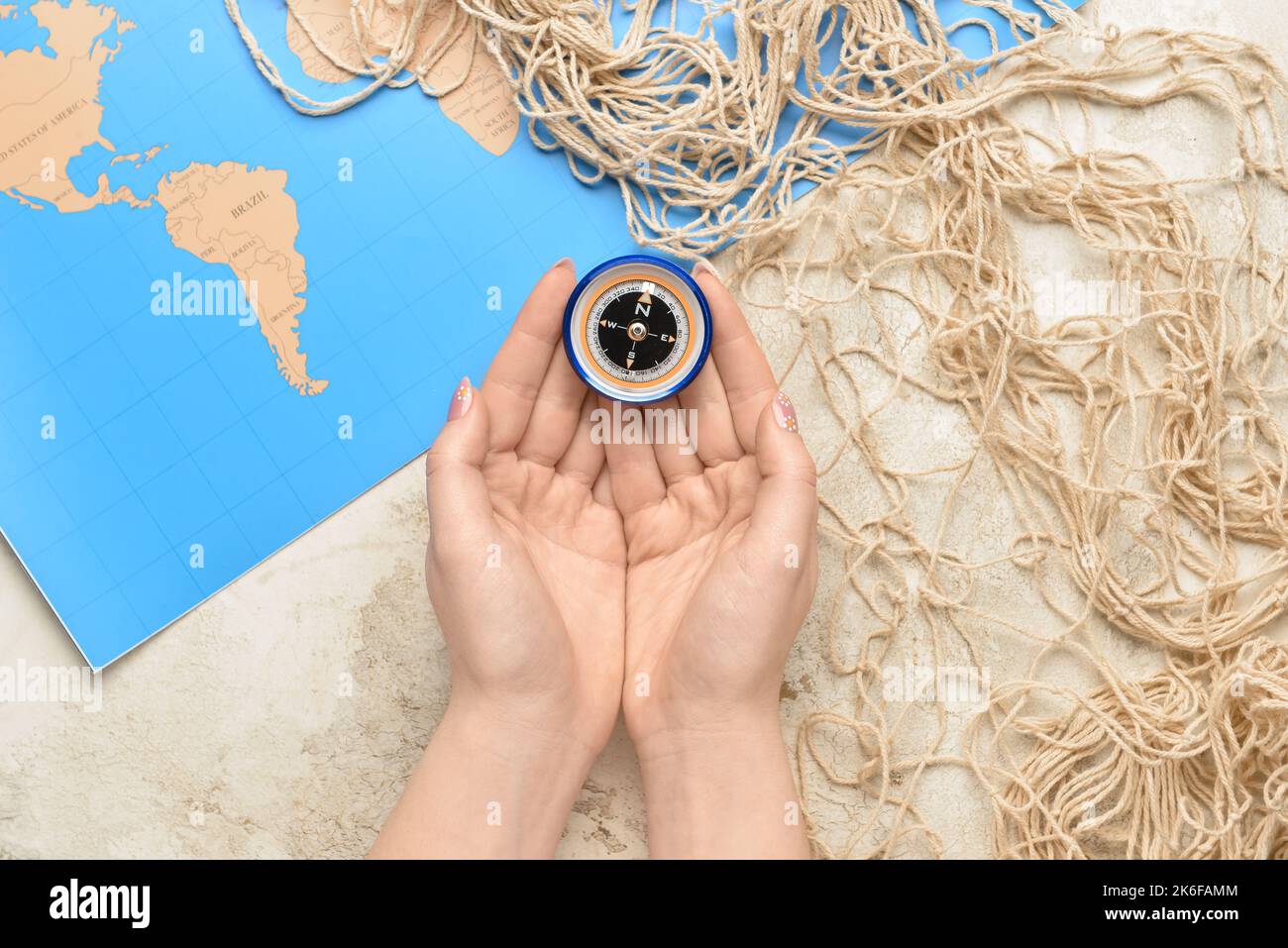 Female hands with compass, fishnet and world map on light background Stock Photo