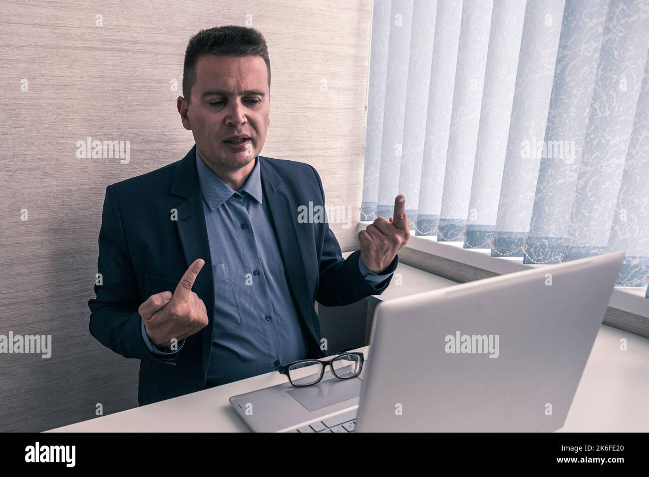 Annoyed mad businessman wearing suit frustrated with online problem, angry stressed male professional using laptop outraged by broken pc, crazy about Stock Photo