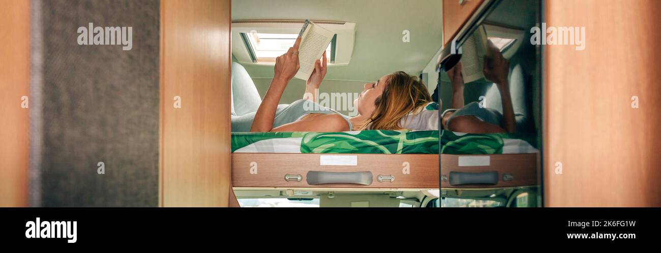 Woman reading book lying on camper van bunk bed Stock Photo