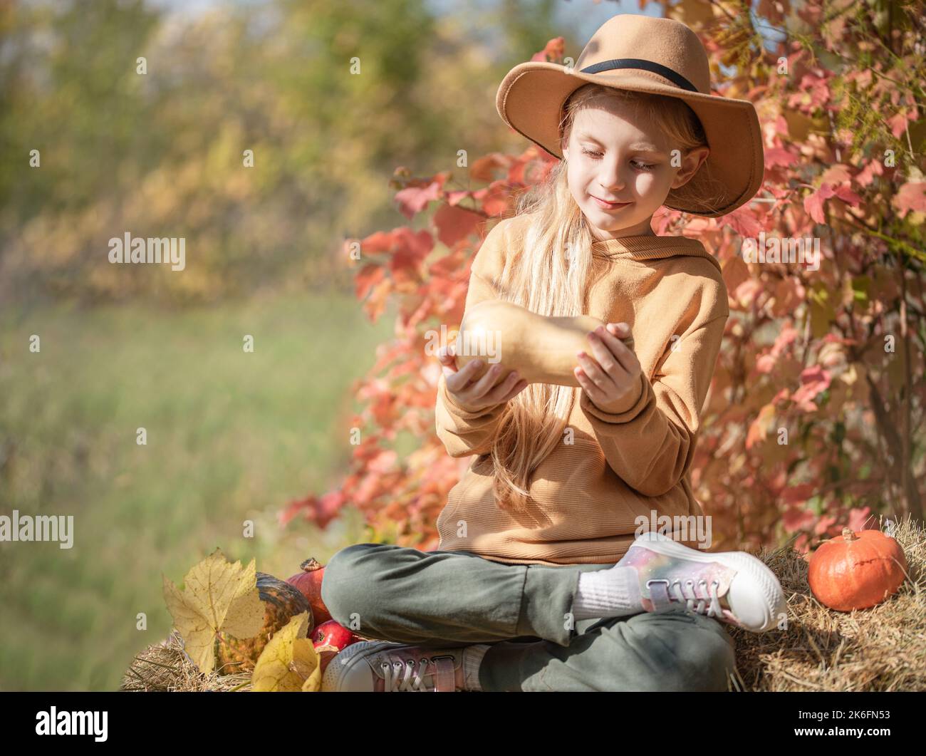 Little girls sitting among hay bales and pumpkins in the autumn garden ...