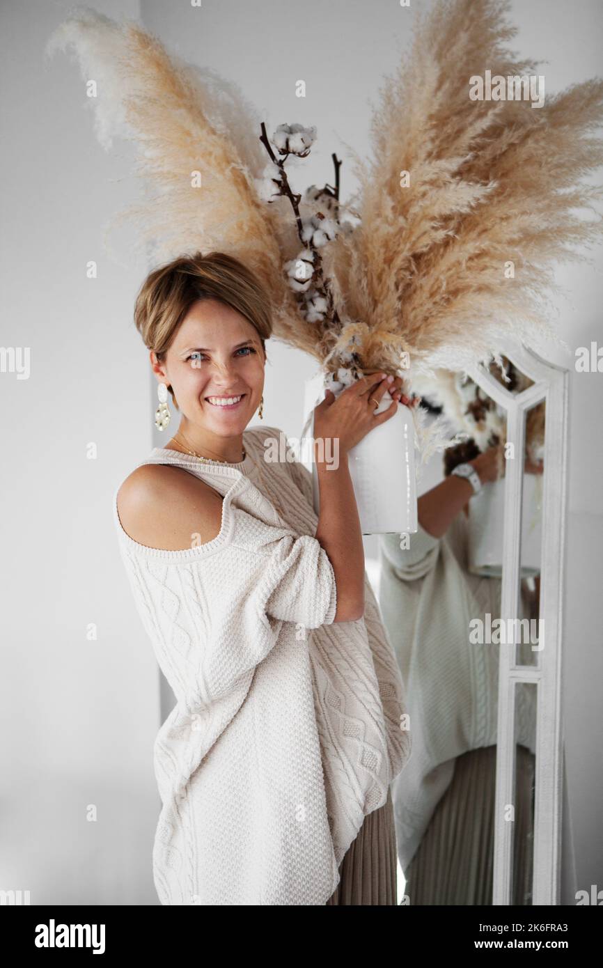 Beautiful interior designer decorates the new house with a bouquet of cotton and dry grass. Woman happy and laughing, having fun feeling, enjoy positi Stock Photo