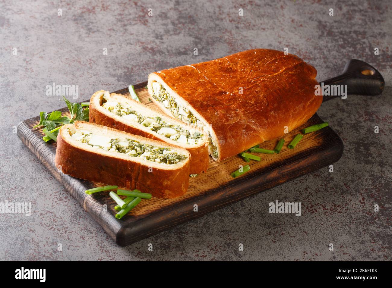 Yeast cake with filling fresh herbs with egg closeup on wooden board on the table. Horizontal Stock Photo