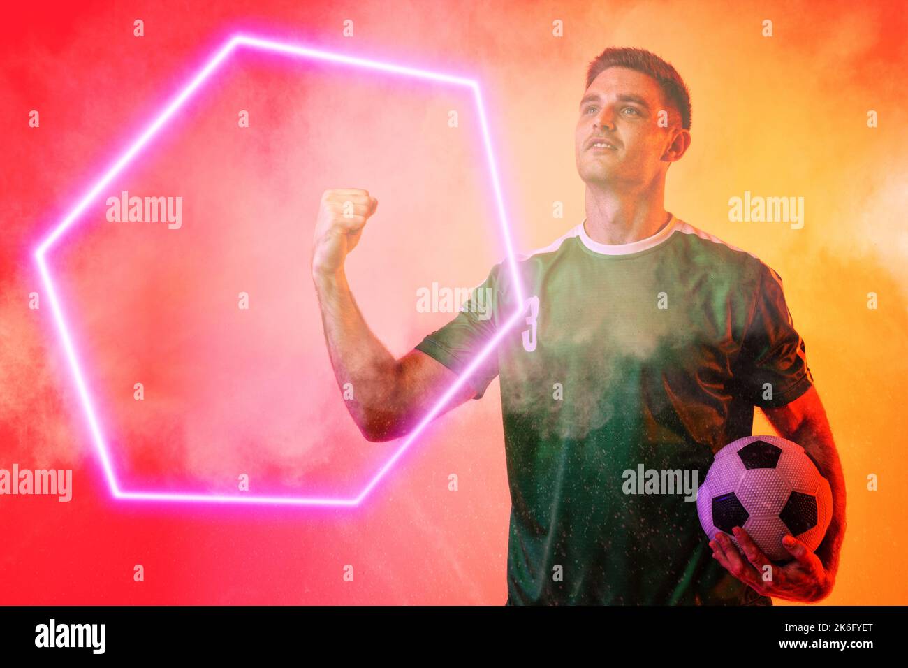 Caucasian male player holding soccer ball clenching fist over illuminated hexagon on neon background Stock Photo