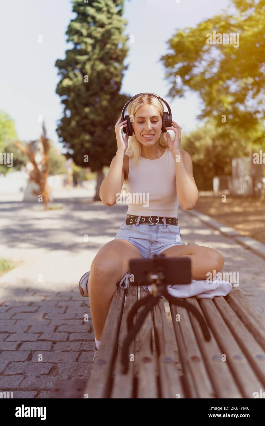 Young girl live streaming from a park bench. Concept of social media blogger, digital content creators. Stock Photo