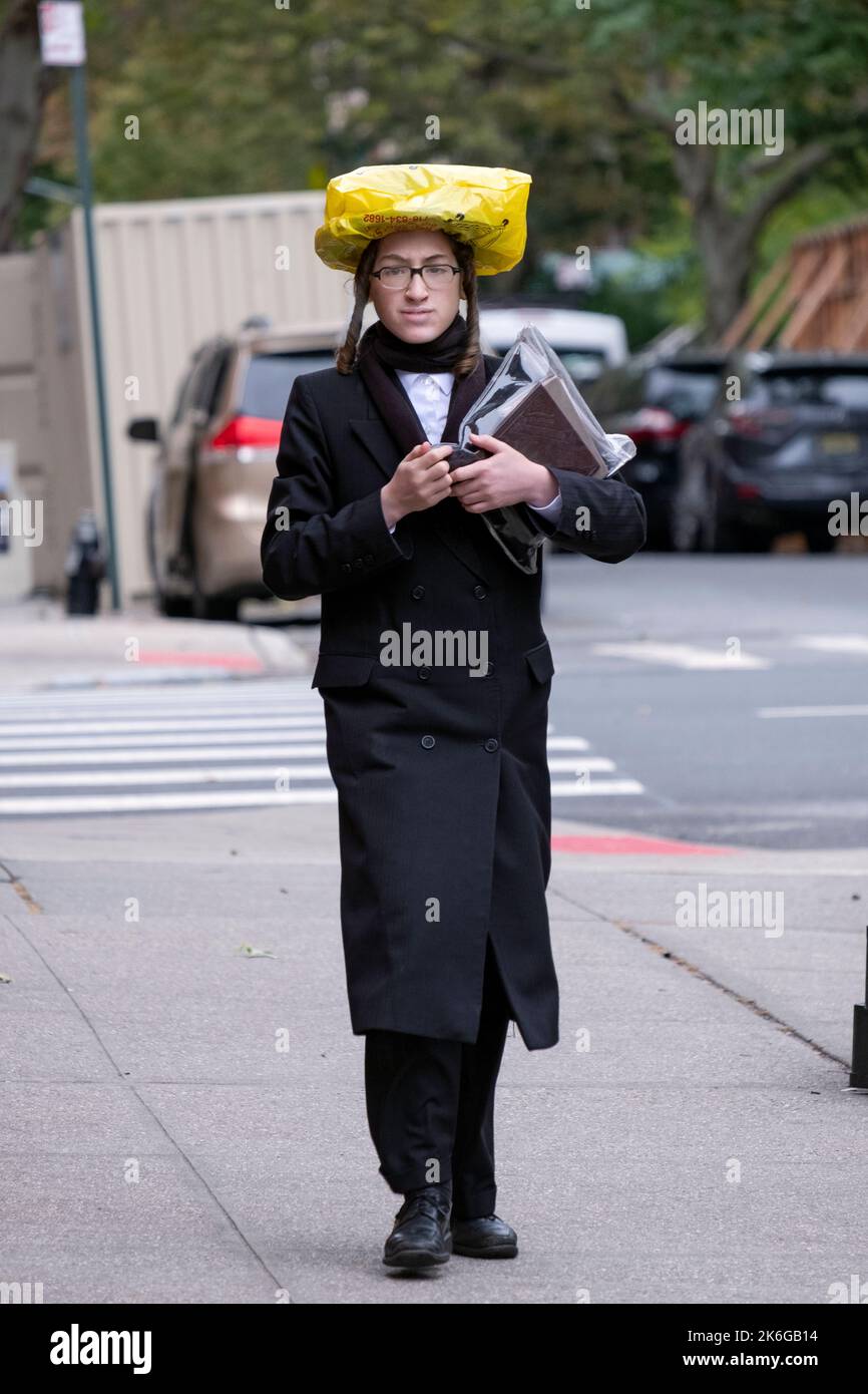 On a drizzly autumn day a Hasidic Jew protects his hat wearing and improvised covering. In Williamsburg, Brooklyn, New York City. Stock Photo
