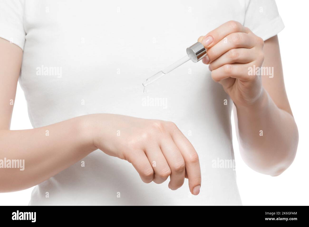 Cropped shot of a woman in white t-shirt holding a pipette with serum, isolated on white. Nice short natural nails. Stock Photo