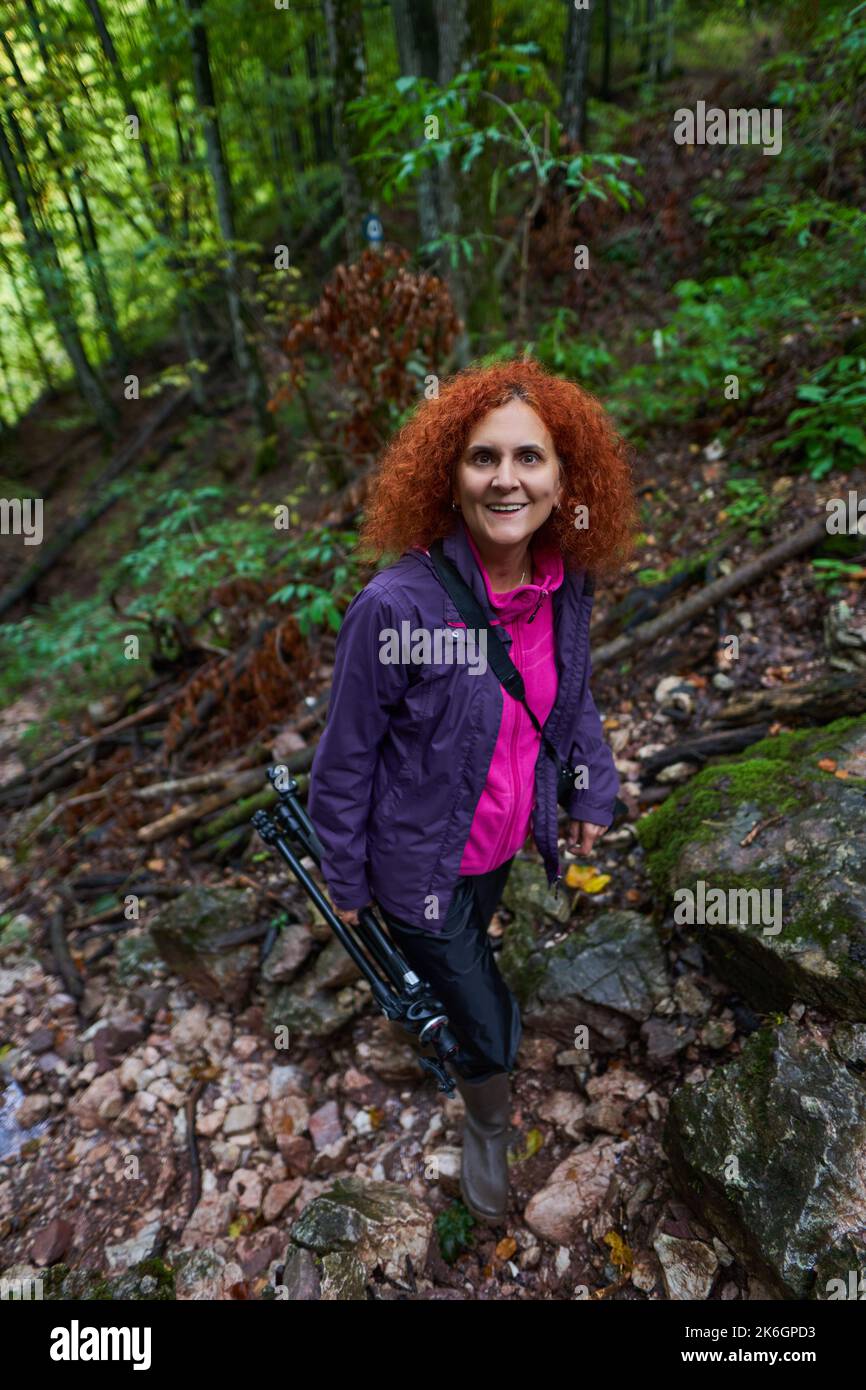 Redhead woman with curly hair and camera hiking on a trail in the ...