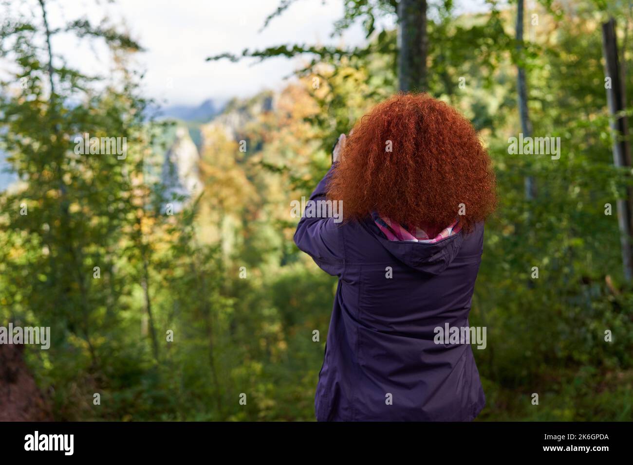 Redhead woman with curly hair and camera hiking on a trail in the ...