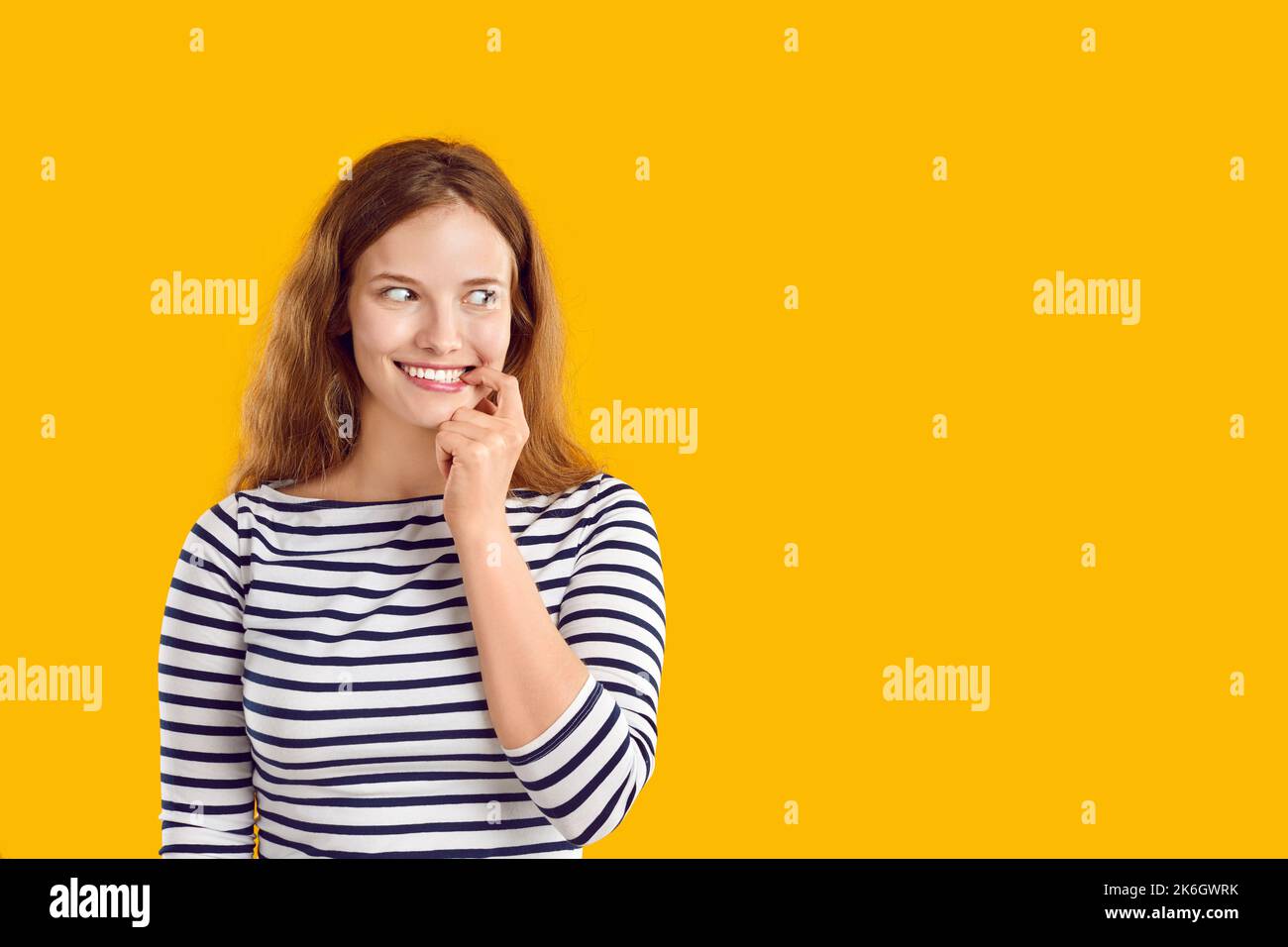 Woman with funny awkward smile on face looks sideways on yellow copy space background Stock Photo