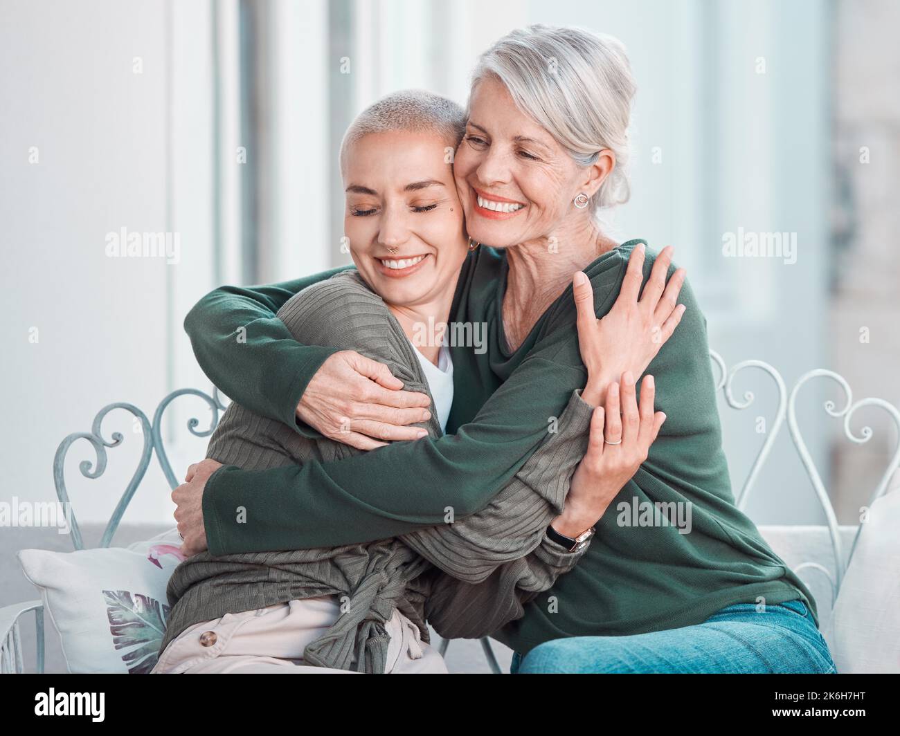 Cheerful senior mother hugging grownup daughter. Loving caucasian mom hugging her daughter while sitting together at home. Senior woman looking happy Stock Photo
