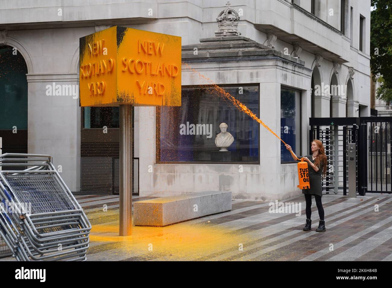A Just Stop Oil protester spray paints a sign outside New Scotland Yard