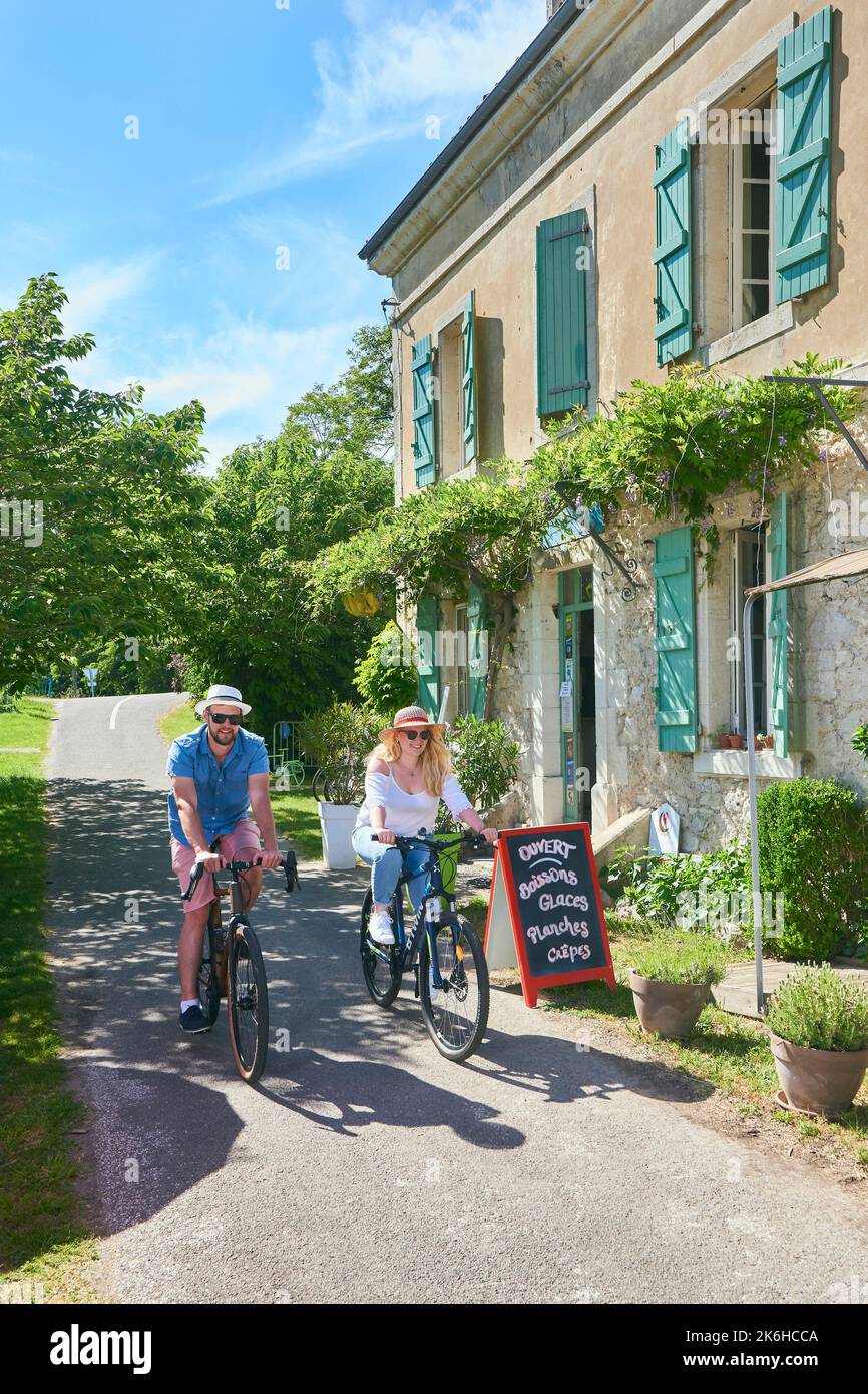 Couple riding bikes on the banks of the Canal du Midi in front of the lock keeper’s house converted into a restaurant and bed and breakfast called “La Stock Photo