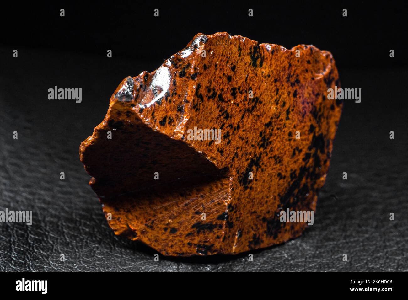 Real shiny specimen of orange Mahogany Obsidian volcanic stone macro isolated on black leather background Stock Photo
