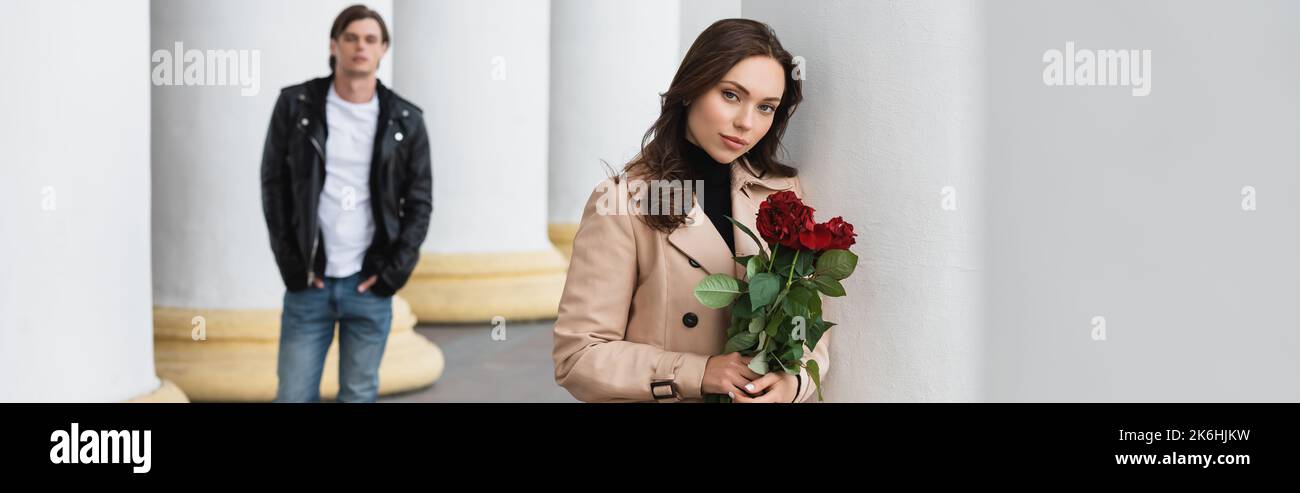 pretty woman in beige trench coat holding red roses near boyfriend on ...