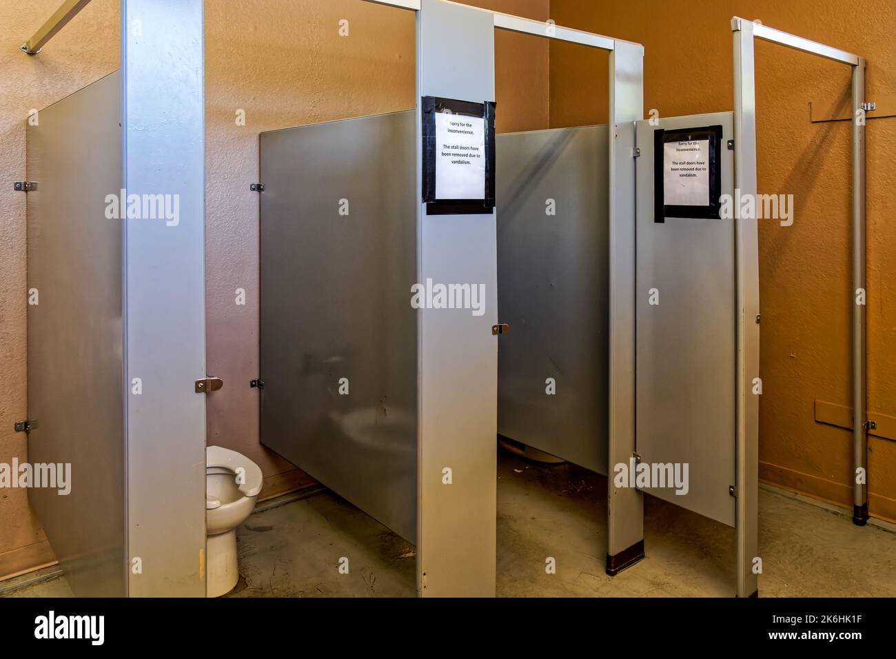 Womens restroom with stall doors removed. Sign says Sorry for the inconvenience.. The stall doors have been rmoved due to vandalism Stock Photo