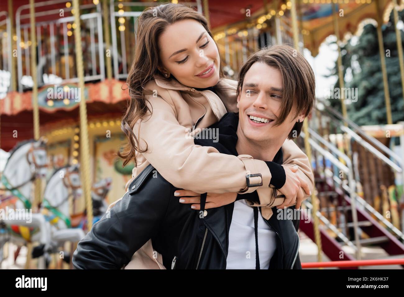 happy woman in trench coat hugging cheerful boyfriend in amusement park ...