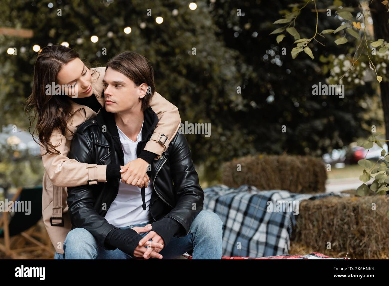 young woman in trench coat hugging stylish boyfriend sitting with ...