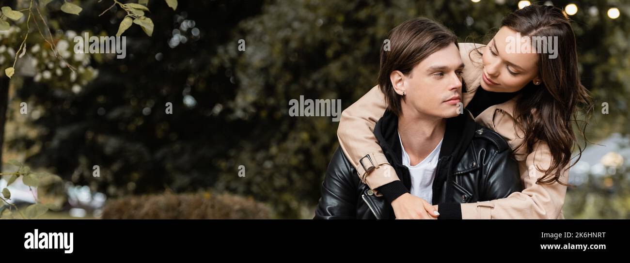 young woman in trench coat hugging stylish boyfriend in park, banner ...