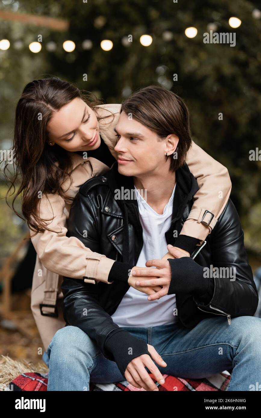 smiling young woman in trench coat hugging stylish boyfriend in park ...