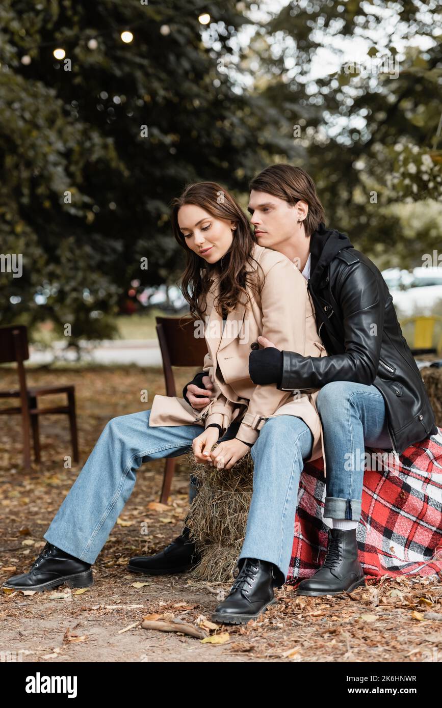 stylish man in black jacket hugging young girlfriend in trench coat ...