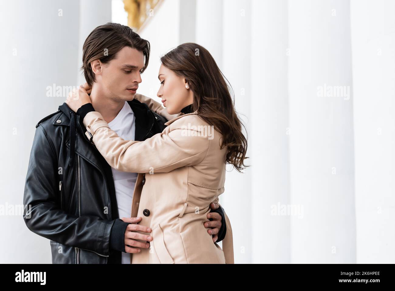 pretty young woman hugging boyfriend in black stylish jacket near white ...