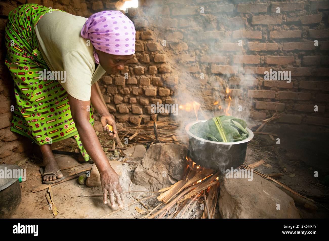 Banana leaves are used to wrap and steam food over a smokey open fire by a woman in Kasese District, Uganda, East Africa. Stock Photo