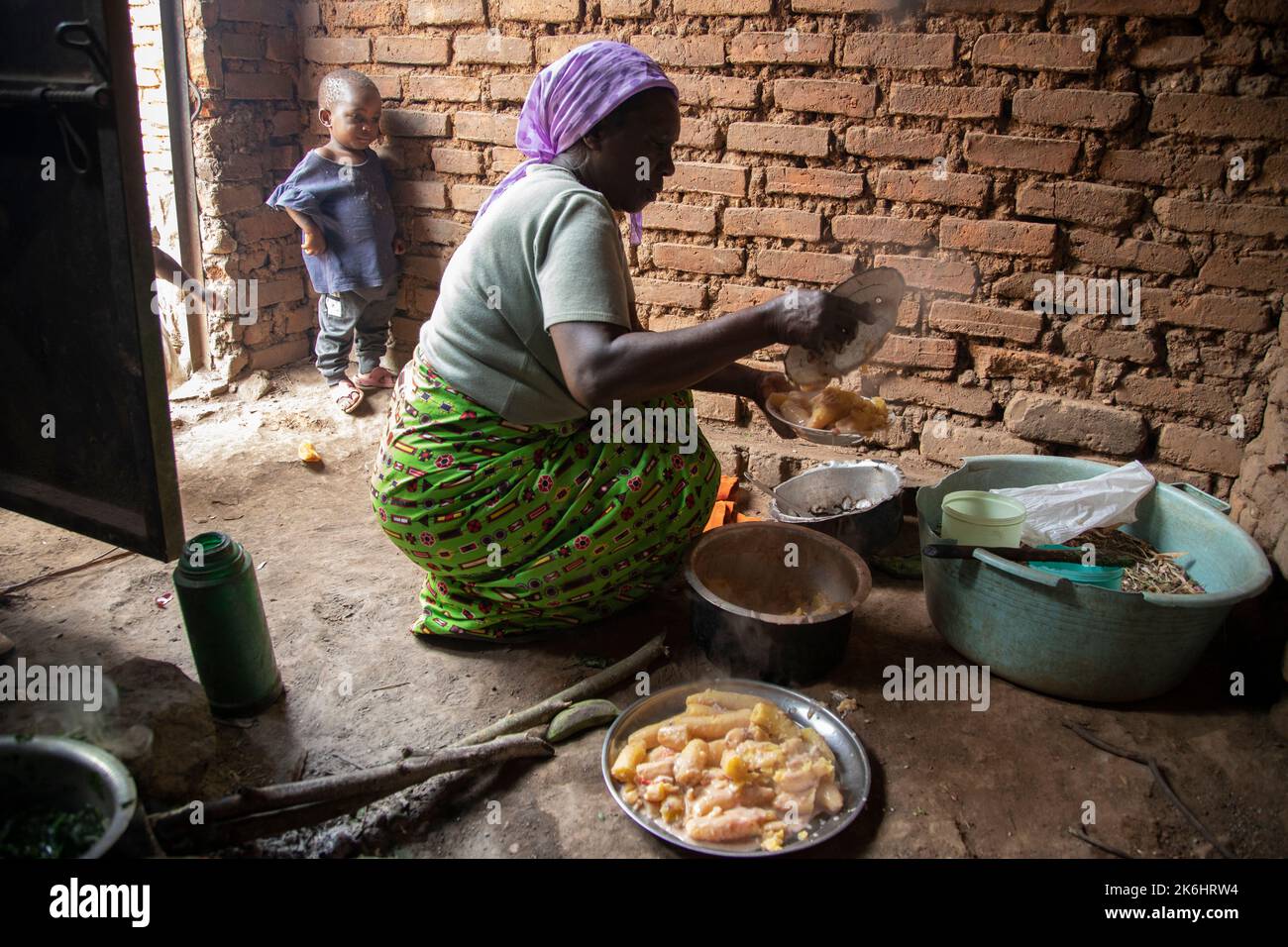 An elderly woman cooks and serves a dish of Ugandan matooke, or starchy