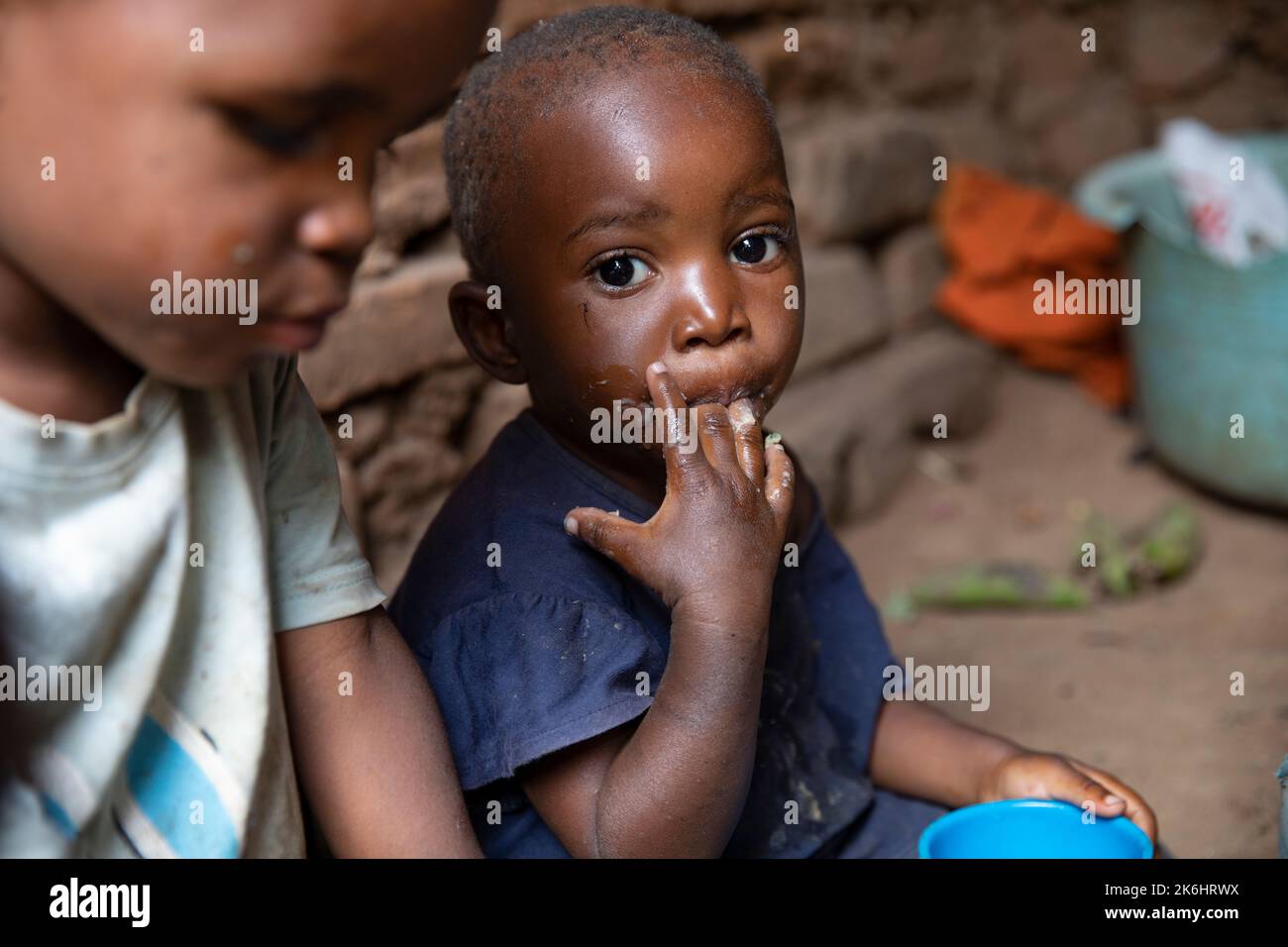 A group of African children eat a meal of starchy bananas and greens with peanut sauce inside their home in Kasese District, Uganda, East Africa. Stock Photo