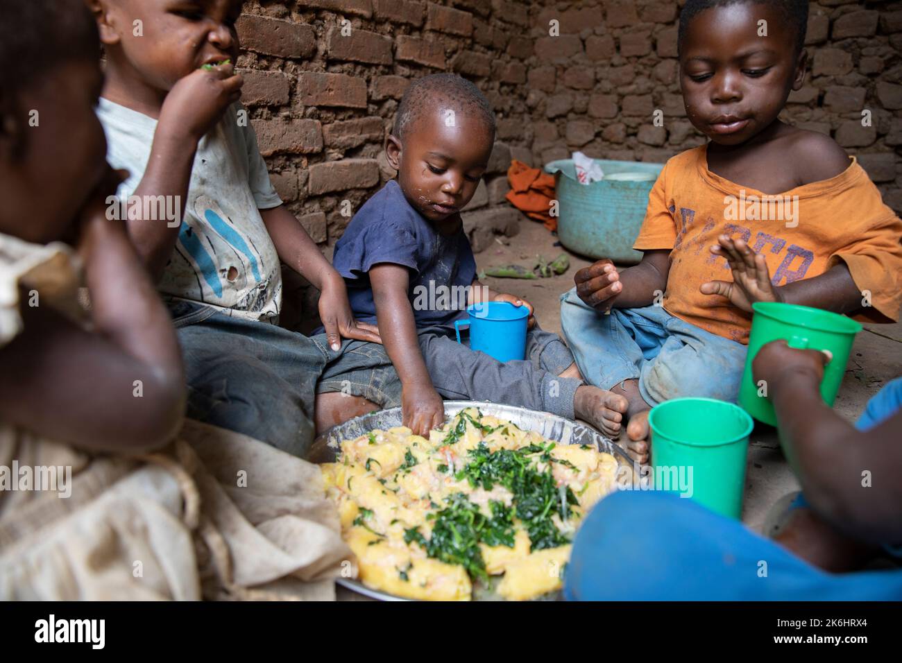 A group of African children eat a meal of starchy bananas and greens with peanut sauce inside their home in Kasese District, Uganda, East Africa. Stock Photo