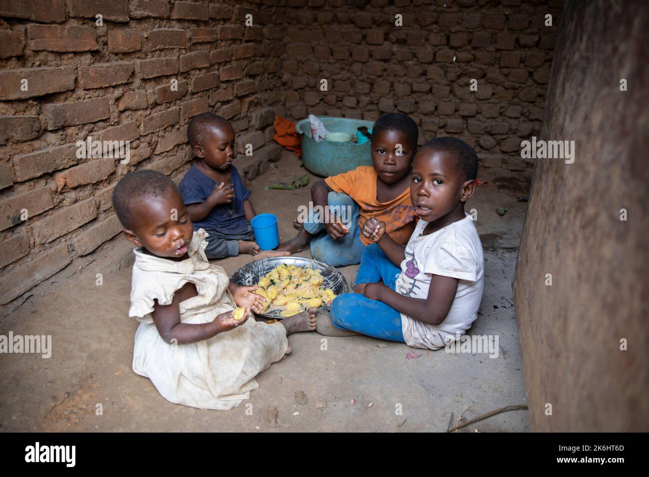 A group of African children eat a meal of starchy bananas and greens with peanut sauce inside their home in Kasese District, Uganda, East Africa. Stock Photo