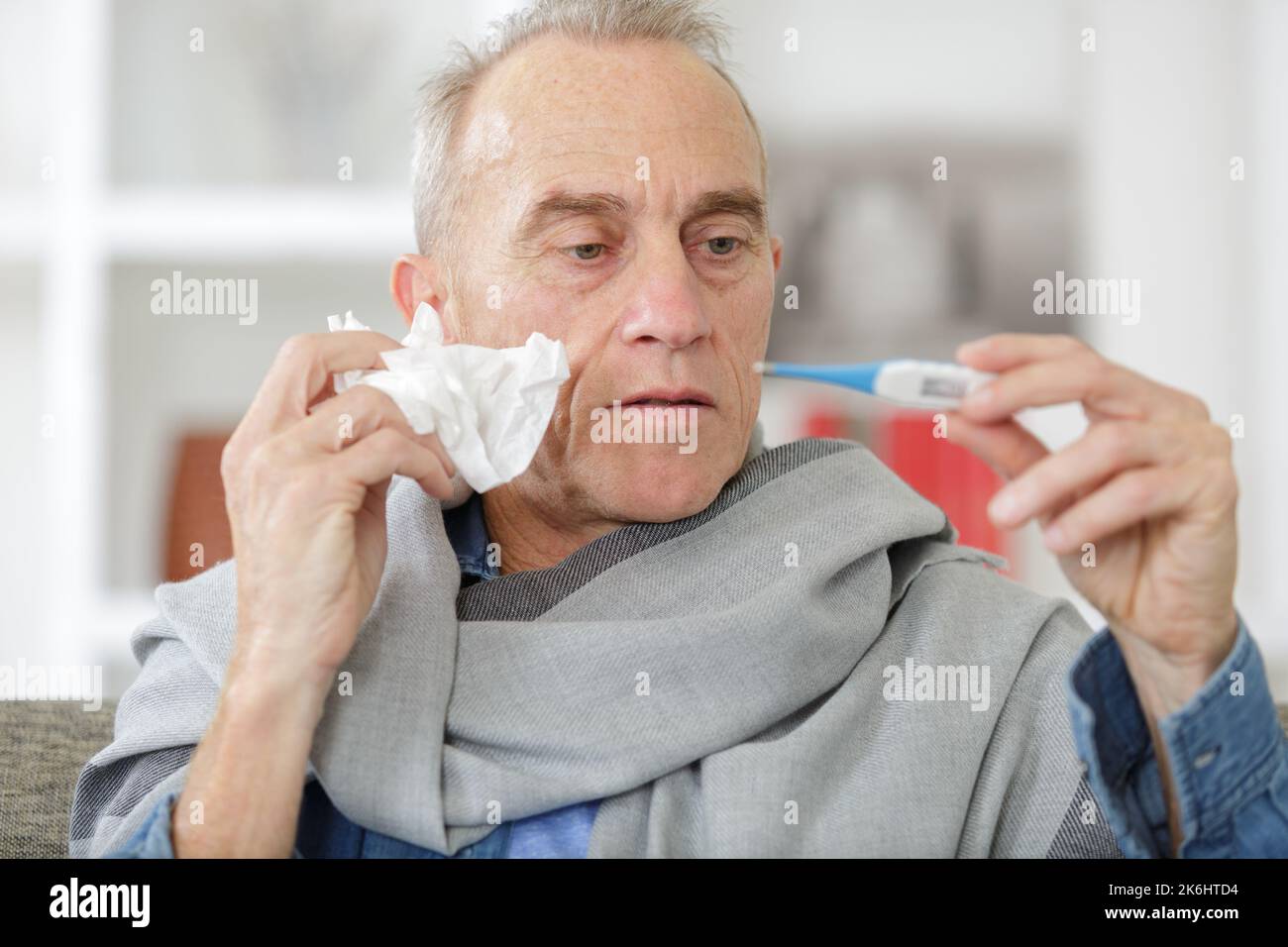 senior man on sofa checking his body temperature with thermometer Stock