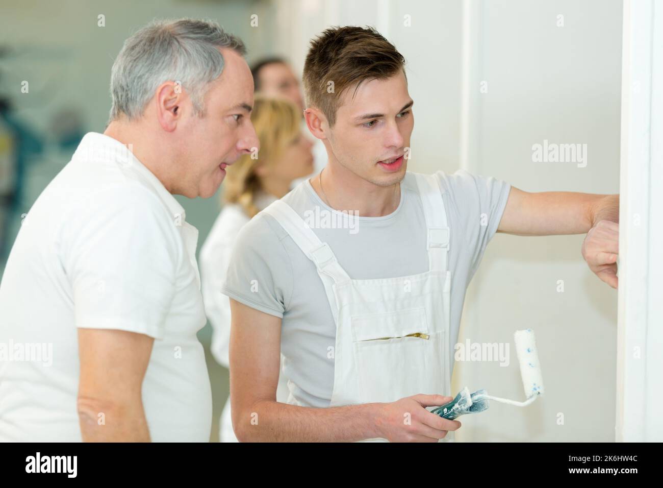 two workers paint a wall in the room using rollers Stock Photo