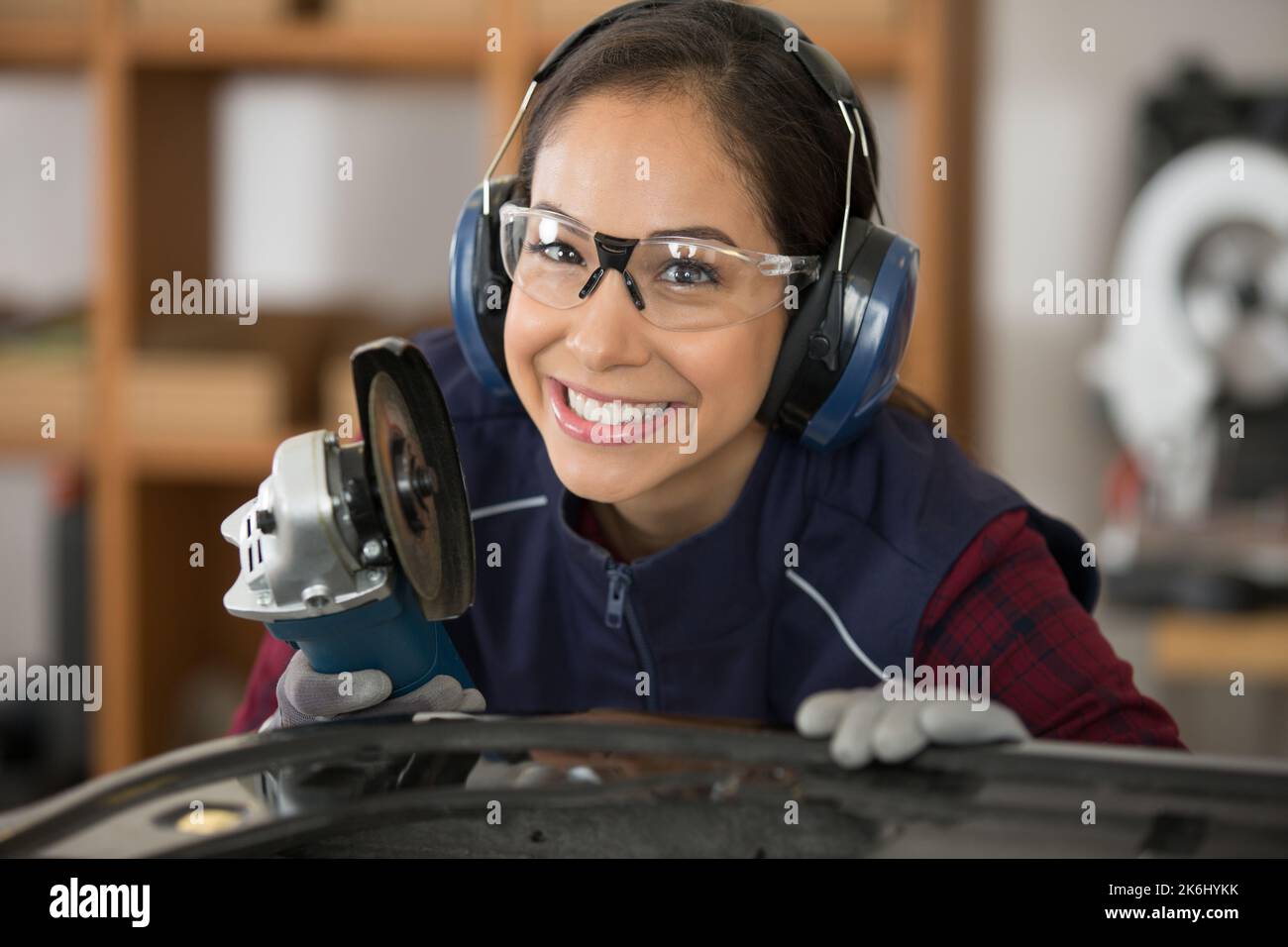 woman wearing ear protection and glasses using electric grinder Stock
