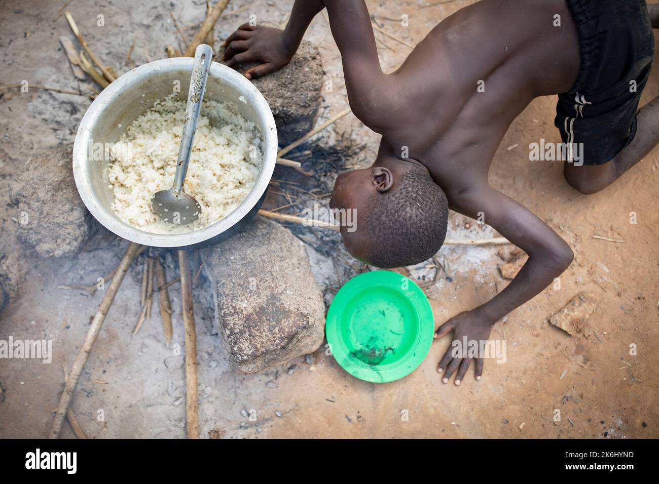 A boy revives a fire by blowing into the firewood while cooking the