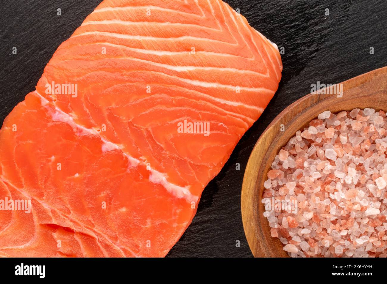 One piece of fresh salmon fillet with salt on slate stone, macro, top