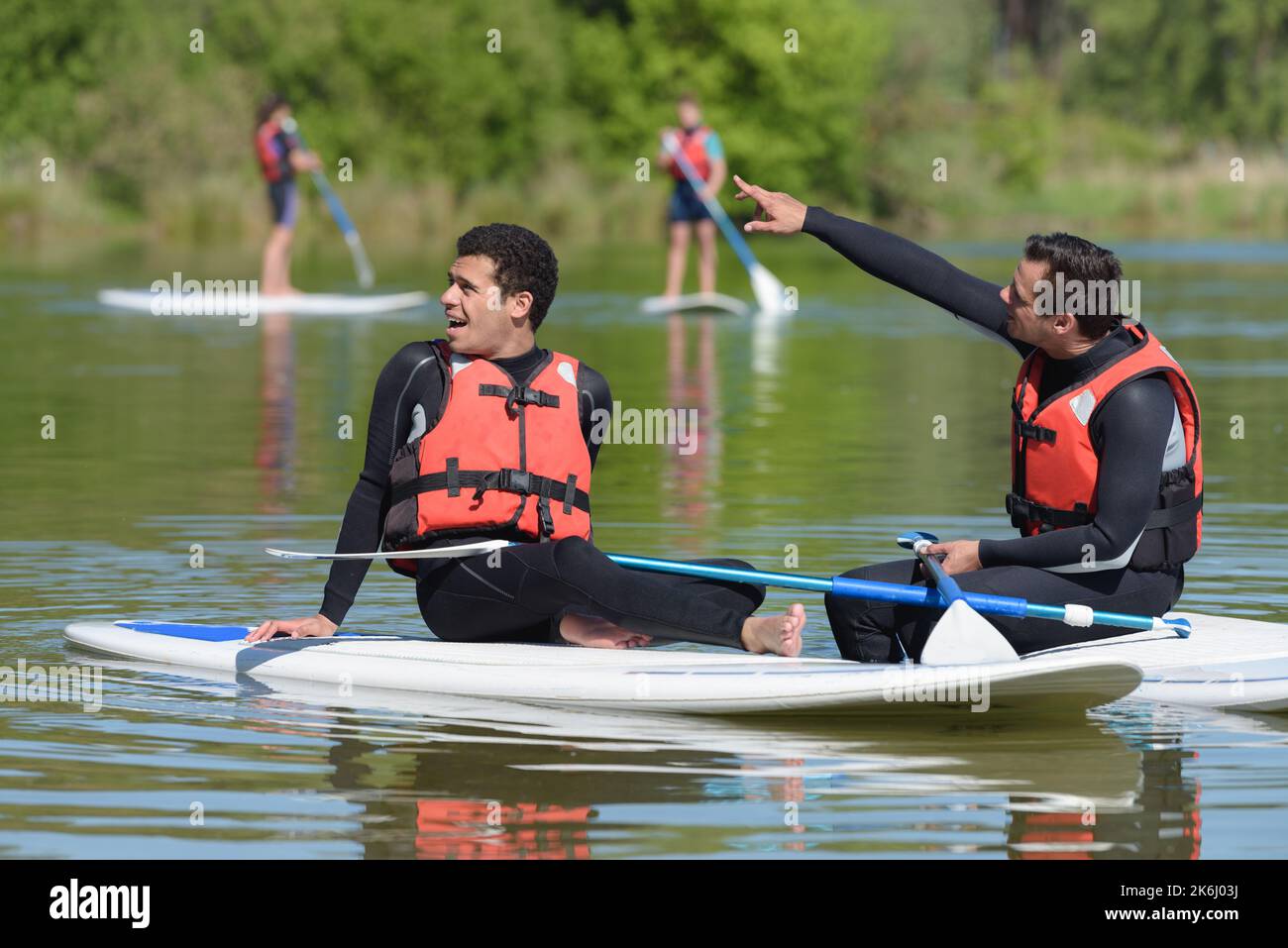 two men relaxing on paddle boards one pointing into distance Stock Photo Alamy