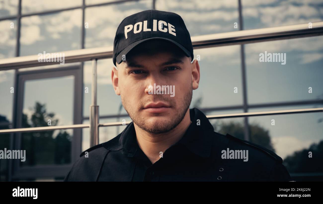 young policeman in cap with lettering police and uniform looking at camera,stock image Stock Photo