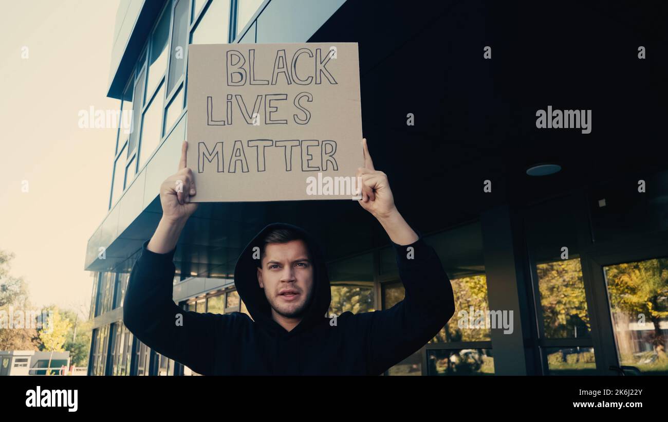 serious young activist in hoodie holding placard with black lives ...